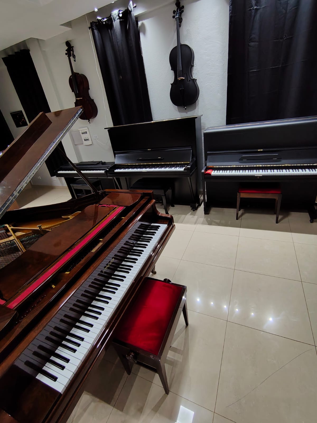 Salão com pianos verticais e violoncelos